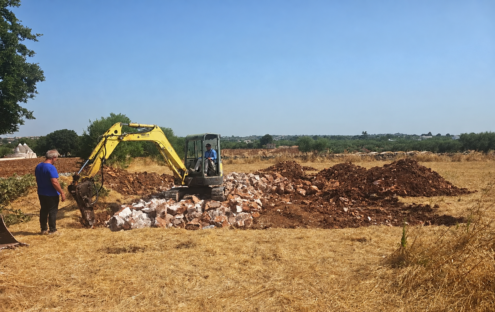 Escavatore al lavoro tra terra rossa e pietra calcarea
